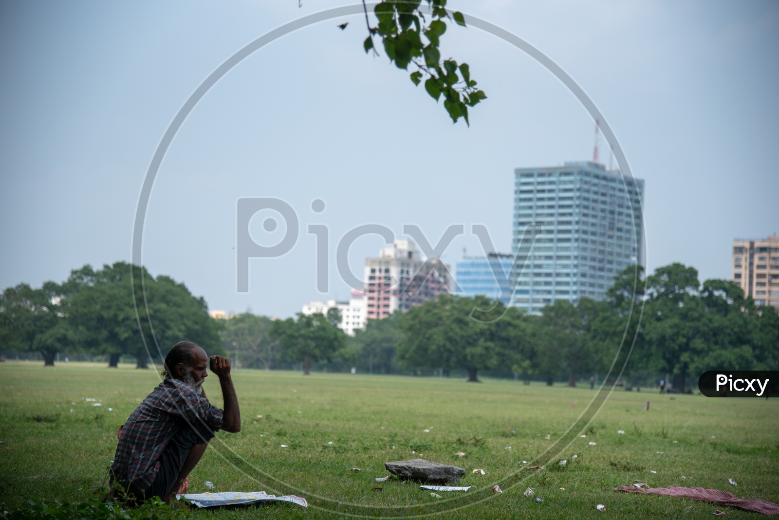 An Old Man reading Paper By Sitting On The Lawn Garden In Maidan
