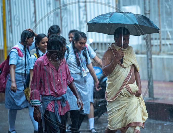A Priest Taking Cover From Rain With  a Umbrella And Walking on Road in Howrah