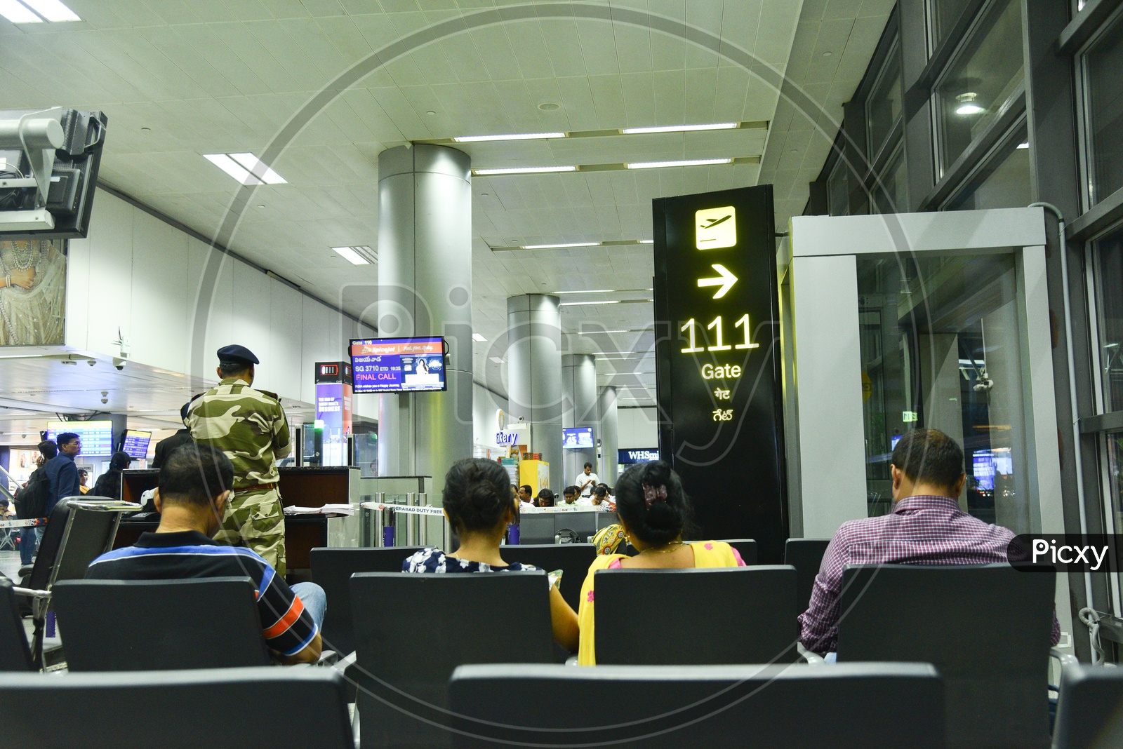 Airport Waiting Lounge  With Passengers Sitting  in  Chairs And Departure Flights  Display Screens