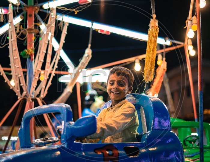 A kid smiling while moving on a dummy car in the carnival
