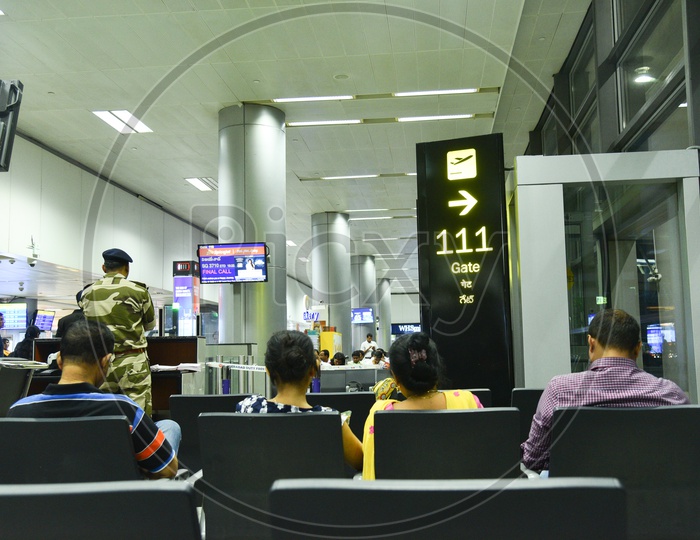 Airport Waiting Lounge  With Passengers Sitting  in  Chairs And Departure Flights  Display Screens