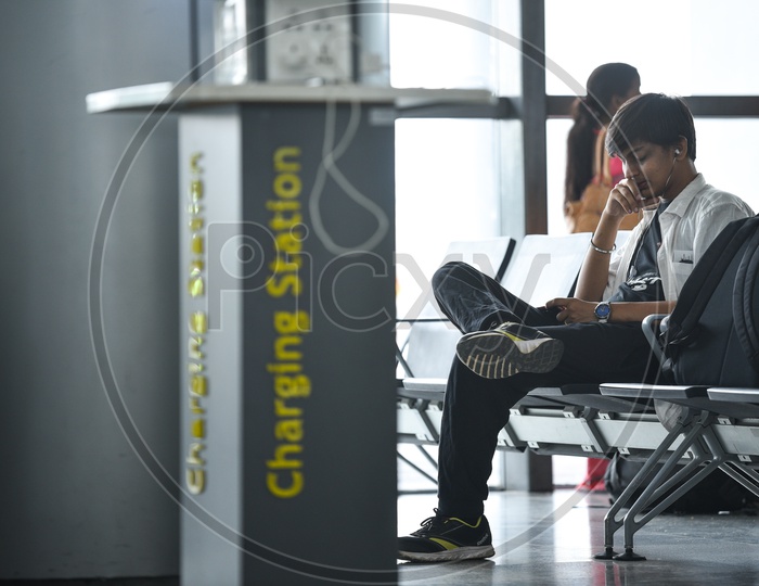 A Young Man  Watching Something In His Smart Phone  By Waiting In  A Waiting Lounge  At  Airport