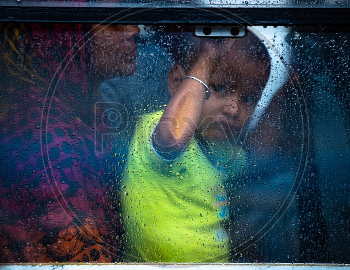 A Small  Child Looking Through The  Window Glass Of a   Bus While The  Rain Lashing Outside