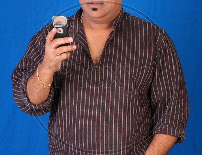 Portrait Of a Indian Man Using Mobile Phone  Or Tollywood Movie Character Artist In Casual Dress  On an Isolated Blue  Background