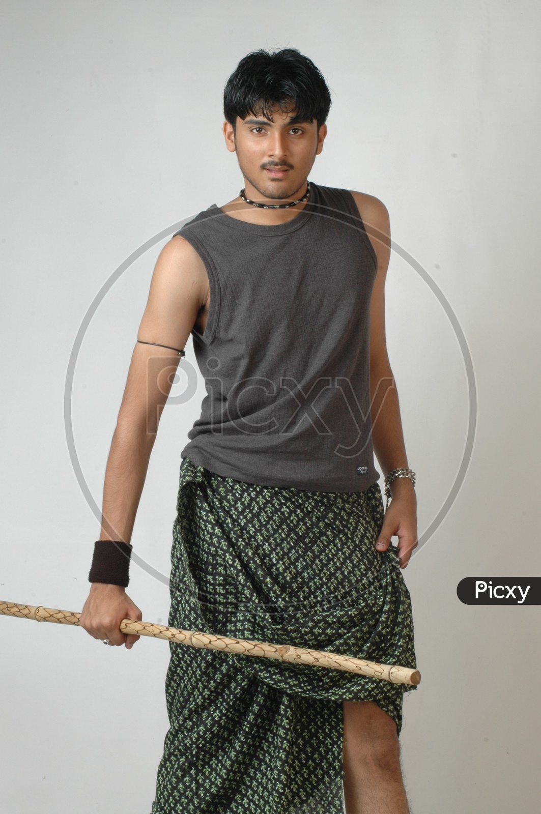 A Young Man in Rural Village Man Attire and Wearing Lungi And  Holding Wooden Stick In Hand On an Isolated White Background