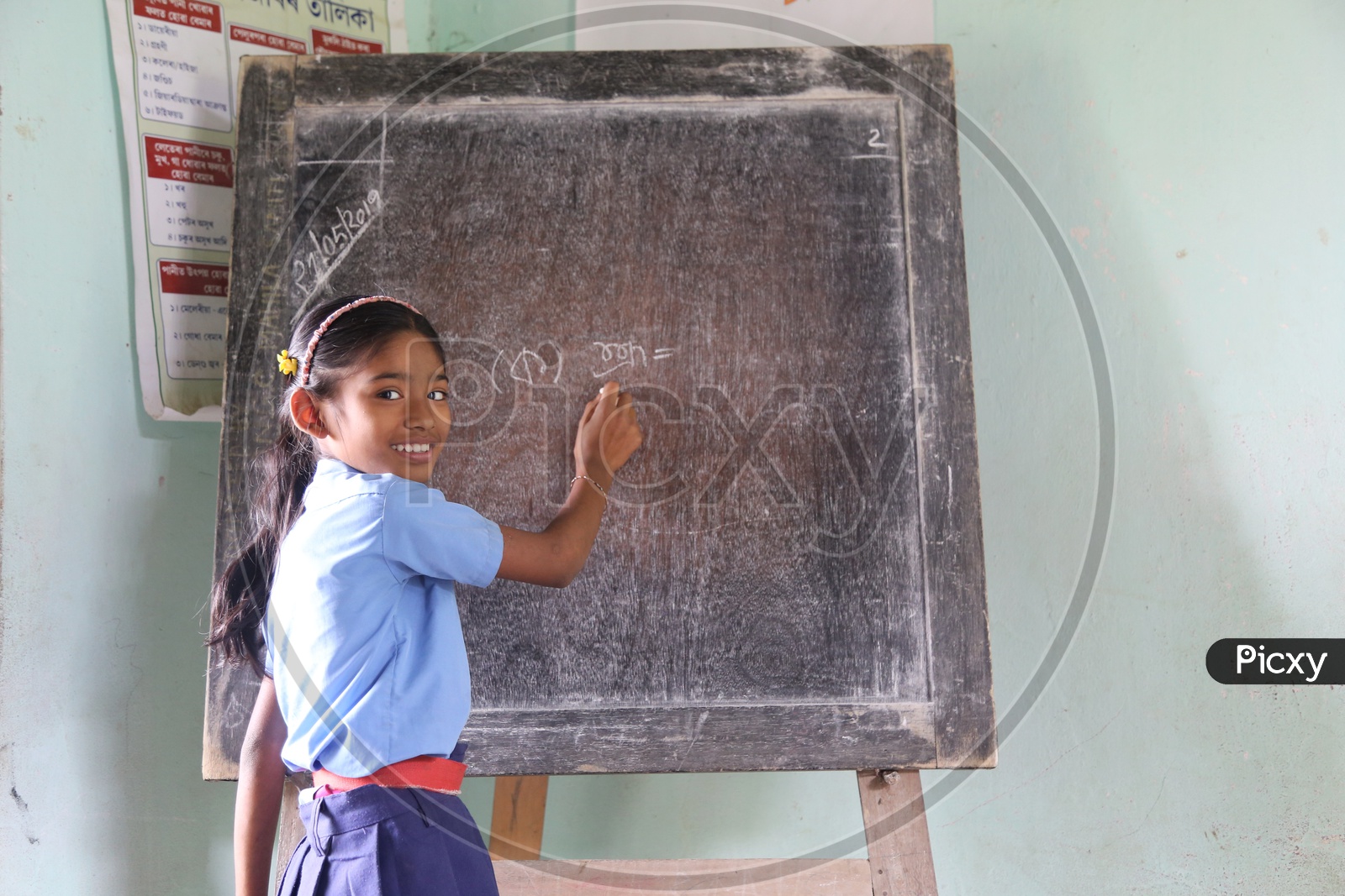 A  Girl Student  Writing On The  School Blackboard in A Classroom