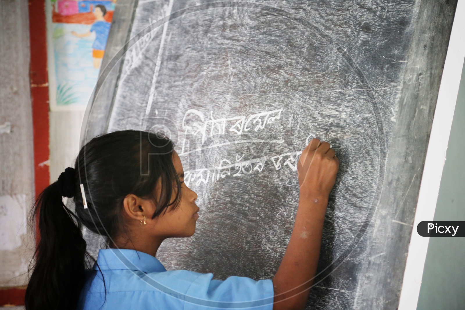 A  Girl Student  Writing On The  School Blackboard in A Classroom