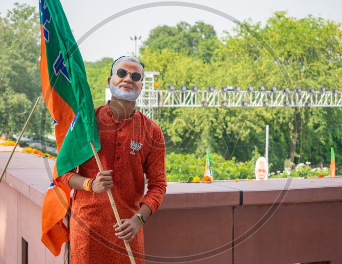 A man wearing mask of Narendra Modi and holding flags of Bhartiya Janta Party(BJP)