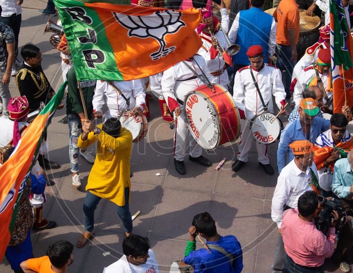 A man dancing and holding Bhartiya Janta Party's(BJP) flag and a band playing drums