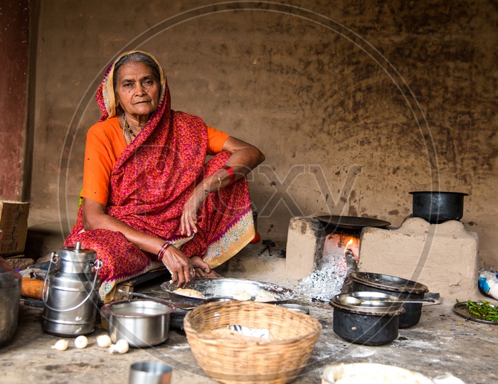 An Indian Old Woman  Making Or Cooking  Food In an Ancient Or Old  Kitchen With Earthen Stove And Wood as Cooking Fuel   in a Rural Village