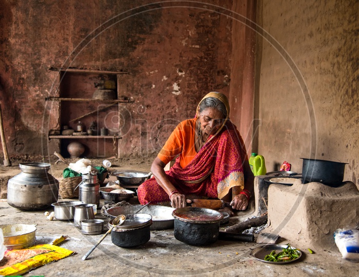 An Indian Old Woman  Making Or Cooking  Food In an Ancient Or Old  Kitchen With Earthen Stove And Wood as Cooking Fuel   in a Rural Village