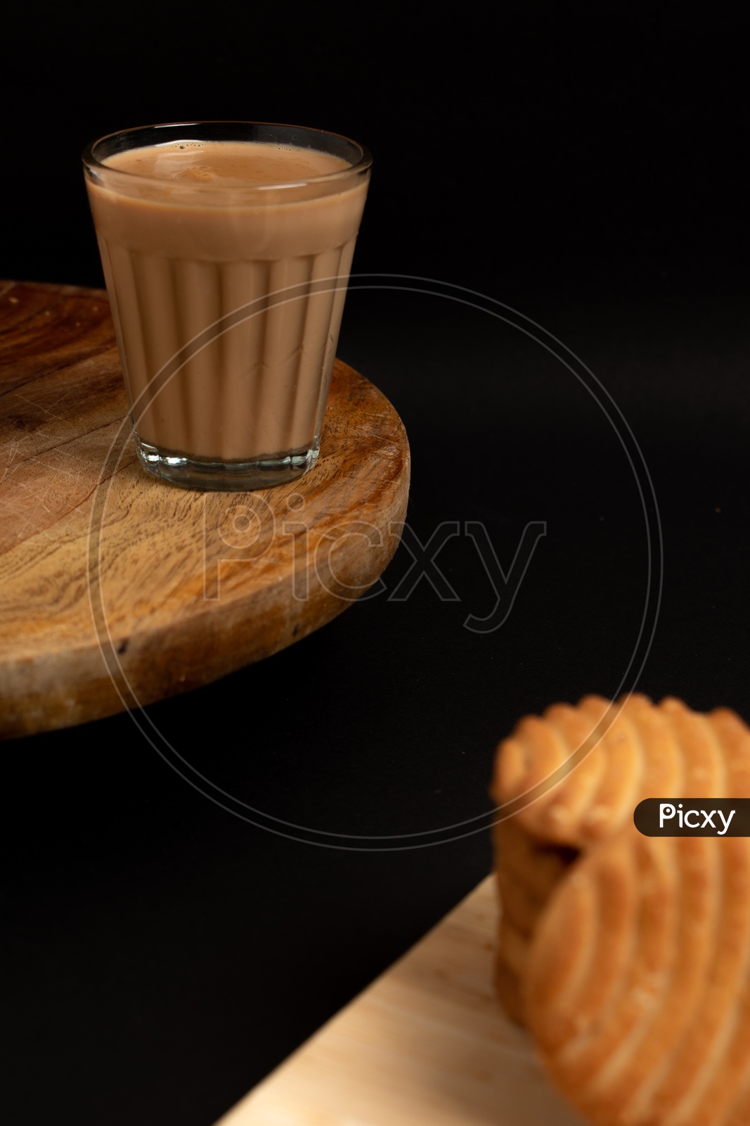 Aromatic beverage  Tea/chai   with Good-day biscuits placed on wooden plates on a black background.