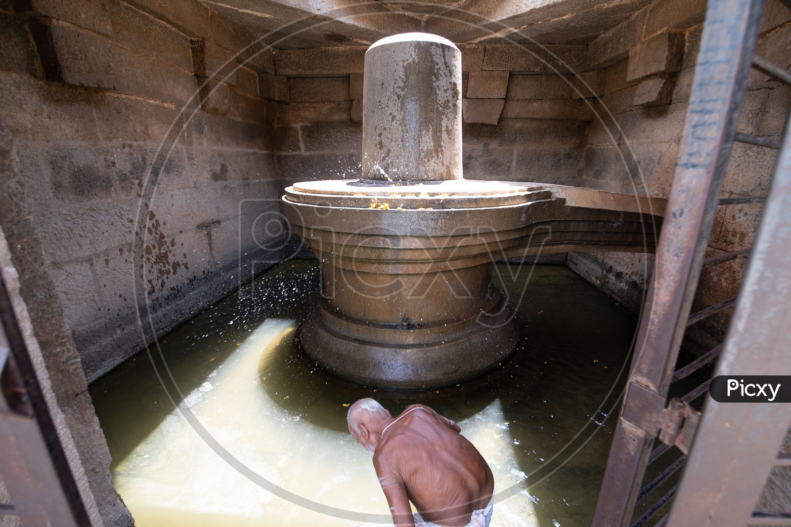 A Priest  Performing  Pooja For the Badavi Linga Statue  Surrounded By  A Pool Of Water In An Ancient Temple In Hampi
