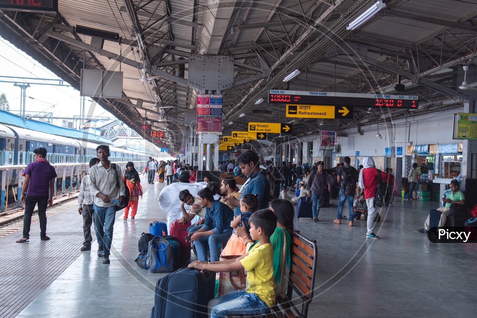 Passengers Waiting By Sitting on Benches With Travel Bags  In a Railway Station Platform