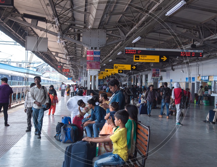 Passengers Waiting By Sitting on Benches With Travel Bags  In a Railway Station Platform