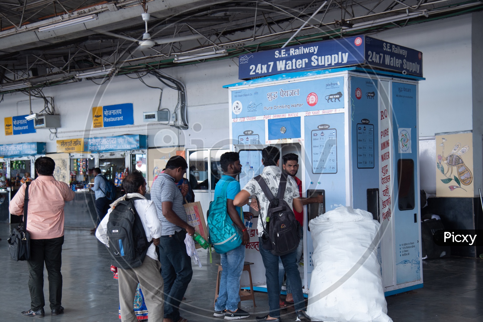 Passengers Filling  Water Bottles At The  Water Supply Points Or Machines By The Indian Railways In a  Railway Station Platform