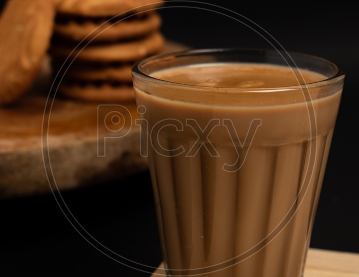 Aromatic beverage Tea/chai  with Good-day biscuits placed on wooden plates on a black background.