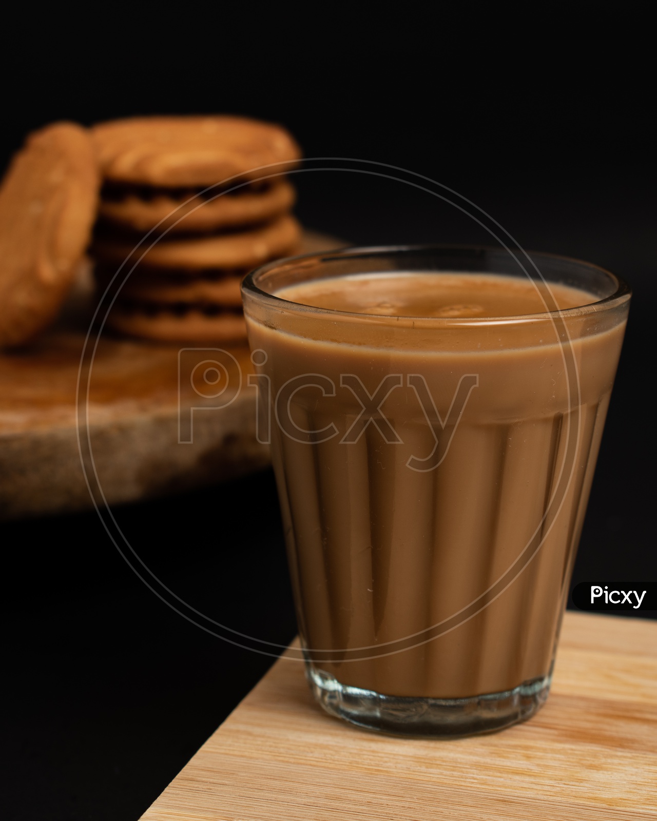 Aromatic beverage Tea/chai  with Good-day biscuits placed on wooden plates on a black background.