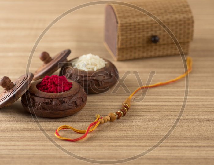 An Elegant Rakhi With Rice Grains And Kumkum  On a Wooden Background
