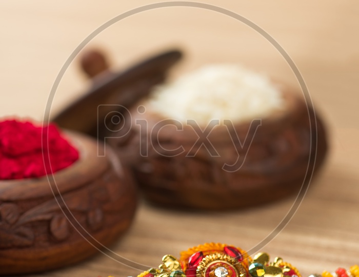 An Elegant Rakhi With Rice Grains And Kumkum  On a Wooden Background