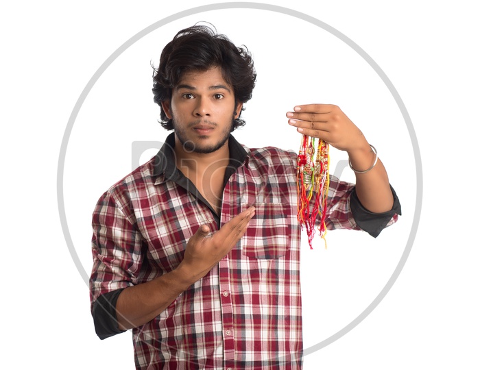 A Young Indian Man Holding Elegant Rakhis In Hand Posing Over a White Background