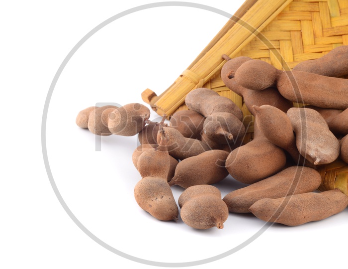 Tamarind Or Sweet Tamarind Fruit in a Wooden Weaved Basket on an Isolated White Background