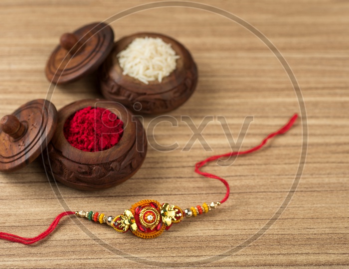 An Elegant Rakhi With Kumkum And Rice Grains On an Isolated Wooden Background