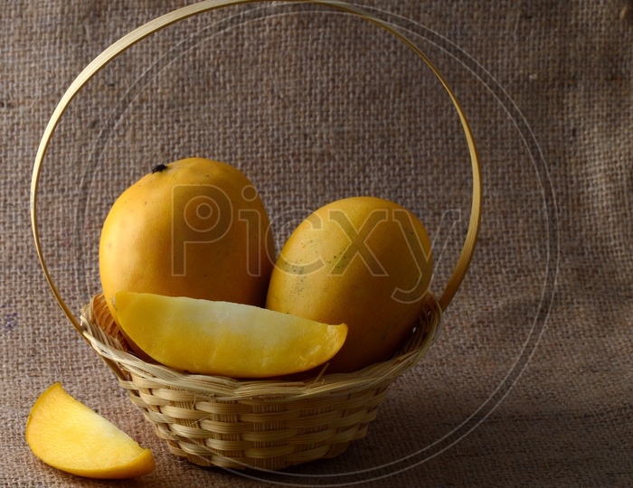 Fresh Ripen Mangoes And Mango Slices in a Bamboo Wood Waved Basket On a Sack Cloth Background