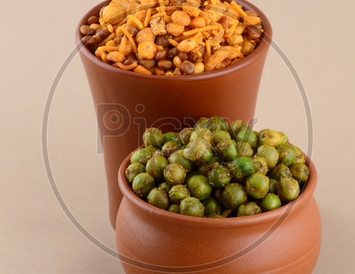 Indian Snack Salty Deep Fried Chivda Or  Mixture and Deep Fried Masala Green Peas  In a Clay Pots  On an Isolated Background