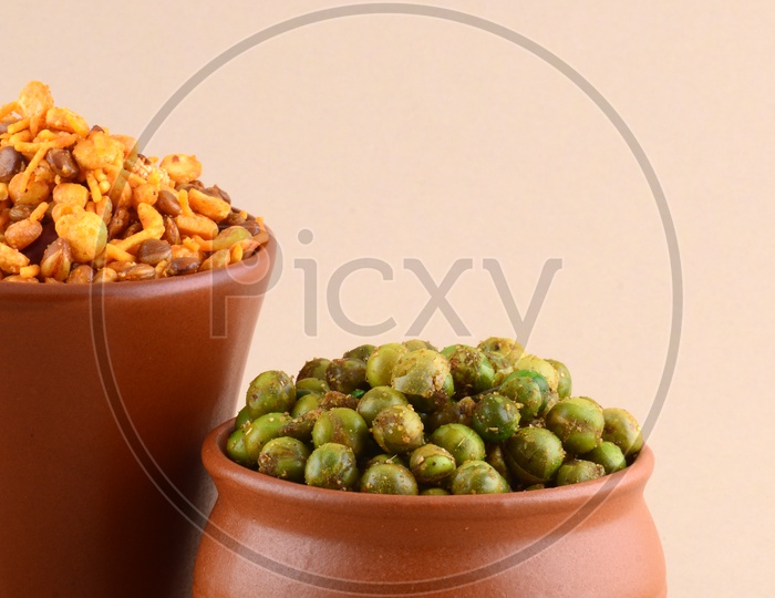 Indian Snack Deep Fried Salty Chivda Or Mixture And  Spiced Fried Green Peas  In a Clay Pot On an Isolated Background