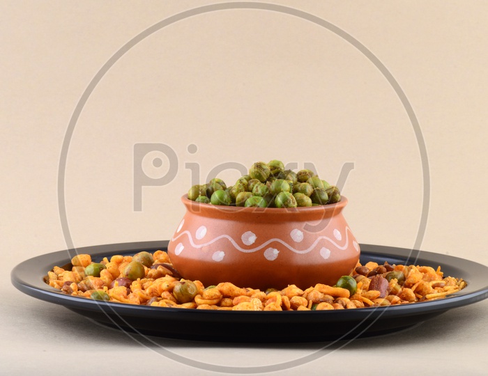 Indian Snacks, Salty Deep Fried Chivda or Mixture  Along With Fried Salty Green Peas in a Clay Pot   on an Isolated Background