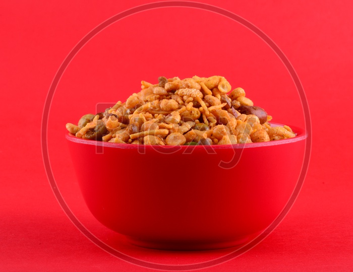 Indian Indian Snacks, Deep Fried Salty  Chivda Or Mixture  In  a Red Bowl On an Isolated Red Background : Mixture (roasted nuts with salt pepper masala, pulses, channa masala dal, green peas) in red bowl on red background