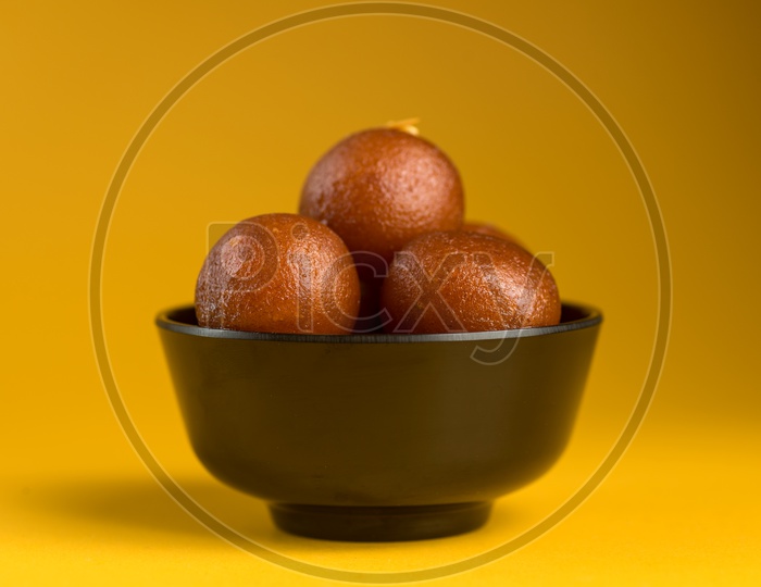 Indian Sweet or Dessert or Savoury Gulab Jamun  in a Bowl On an Isolated Yellow  Background