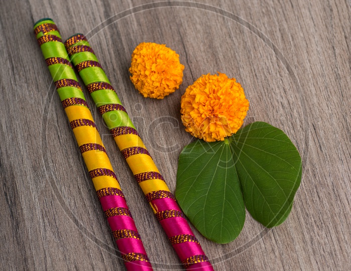 Indian Festival Dussera or Navrathri Symbolic Representation With Dandiya Sticks , Mari Gold Flowers And Golden Leaf ( Bauhinia Racemosa ) on an Isolated Wooden Background
