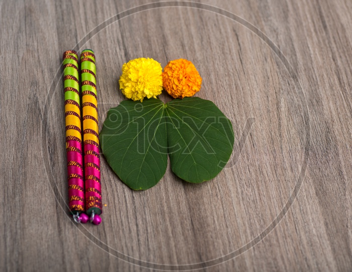 Indian Festival Dussera or Navrathri Symbolic Representation With Dandiya Sticks , Mari Gold Flowers And Golden Leaf ( Bauhinia Racemosa ) On an Isolated Wooden Background