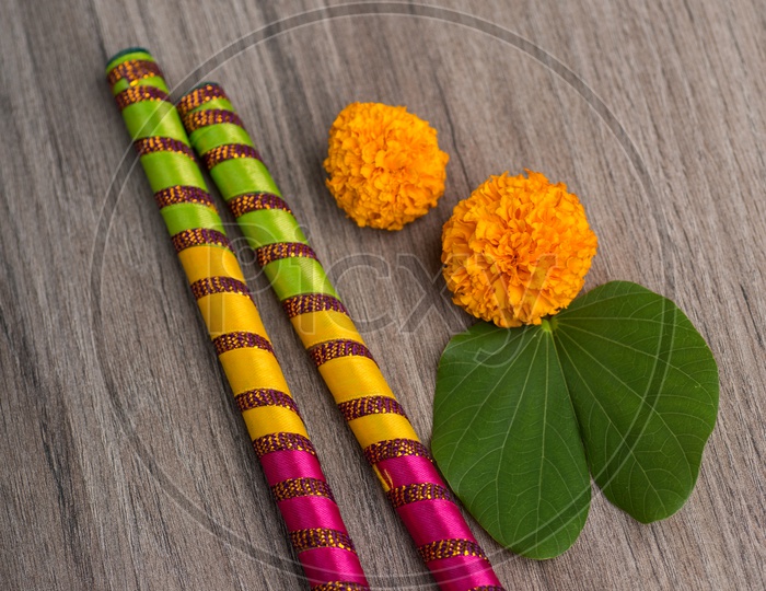 Indian Festival Dussera or Navrathri Symbolic Representation With Dandiya Sticks , Mari Gold Flowers And Golden Leaf ( Bauhinia Racemosa ) on an Isolated Wooden Background