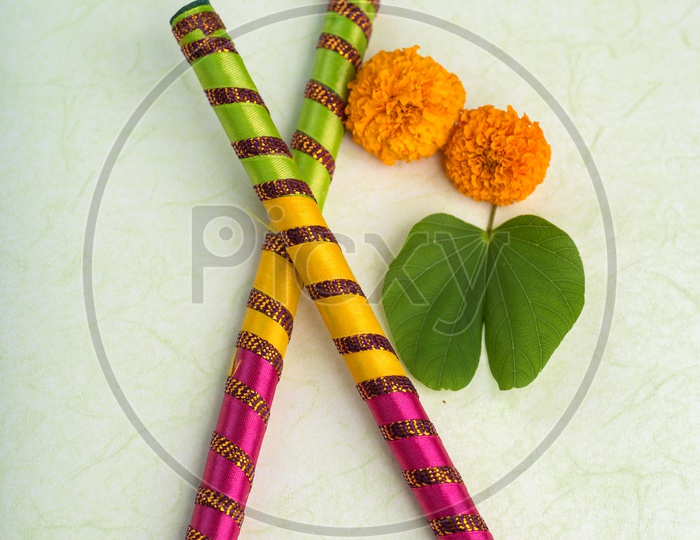 Indian Festival Dussera or Navrathri Symbolic Representation With Dandiya Sticks , Mari Gold Flowers And Golden Leaf ( Bauhinia Racemosa ) on an Isolated White Background