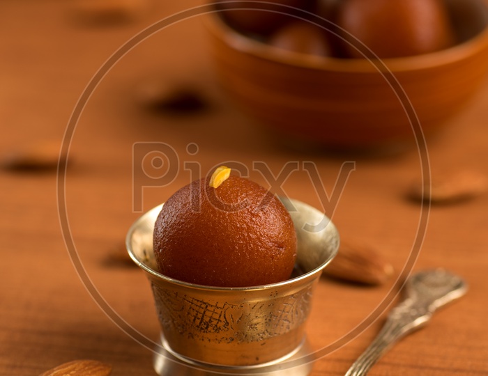 Indian Sweet or Dessert or Savoury Gulab Jamun  Served in an Elegant Bowl Along With a Spoon On an Isolated Wooden Background
