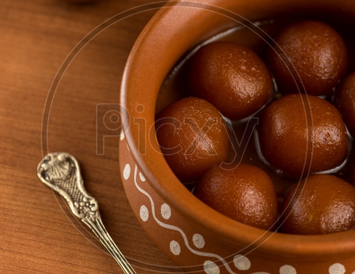 Indian Sweet or Dessert or Savoury Gulab Jamun  Served in an Elegant  Clay  Pot   On an Isolated Wooden Background