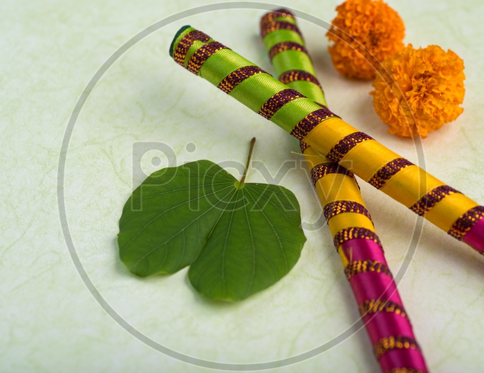 Indian Festival Dussera or Navrathri Symbolic Representation With Dandiya Sticks , Mari Gold Flowers And Golden Leaf ( Bauhinia Racemosa ) on an Isolated White Background