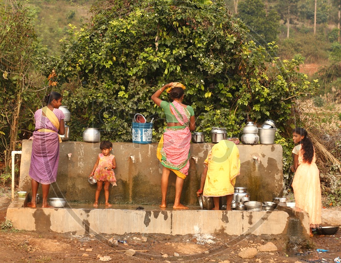 Tribals washing utensils at water taps.