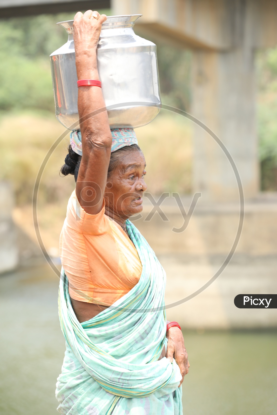 A Rural Village Old Woman  Carrying Water Vessel On Her Head
