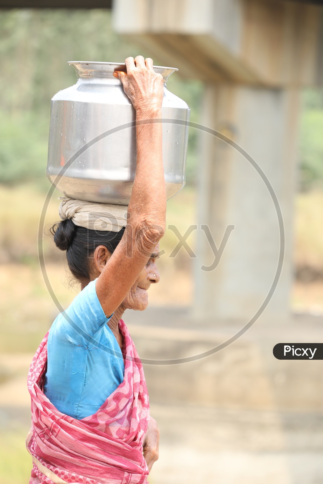 An Old Woman Carrying Water Vessel On Her Head  in a Rural Village