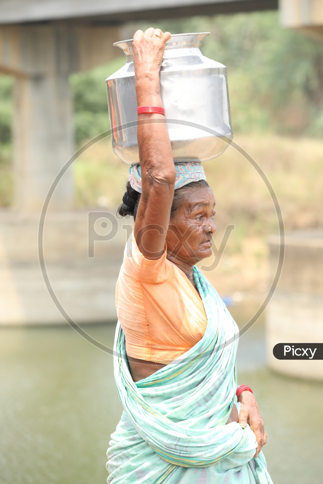 A Rural Village Old Woman  Carrying Water Vessel On Her Head