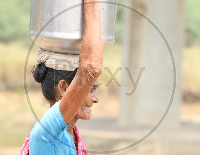 An Old Woman Carrying Water Vessel On Her Head  in a Rural Village