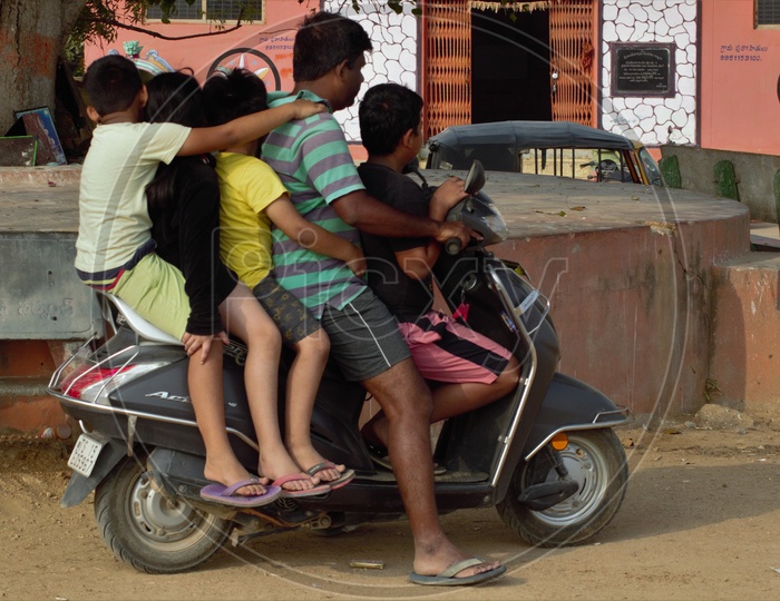 A Man Riding Scooty or Moped With Four Children along With Him