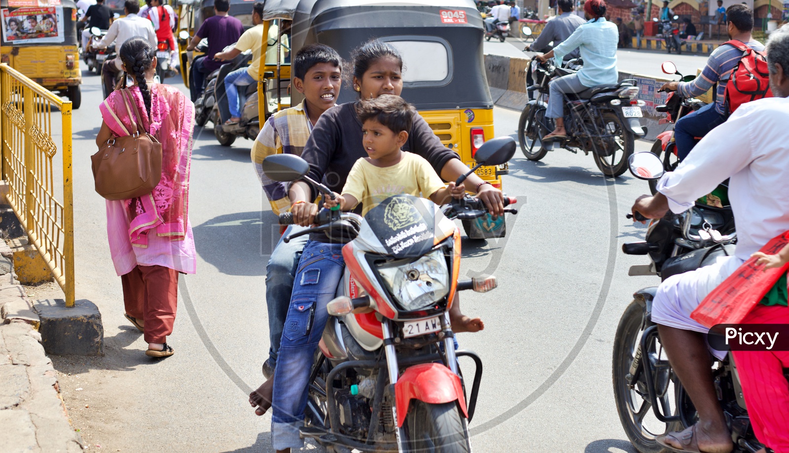 Girl riding a geared motor cycle with 3 members on the bike and riding against the traffic.
