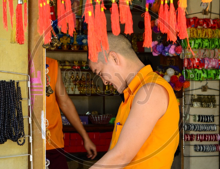 A buddhist monk checking out souvenirs at a shop.