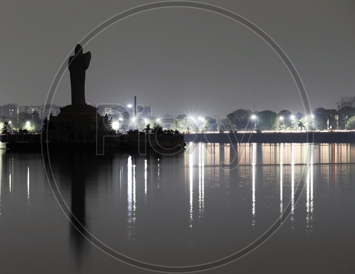 Silhouette Of Gautham Buddha Statue in Hussain Sagar Lake With Street Lights On Roads In Background