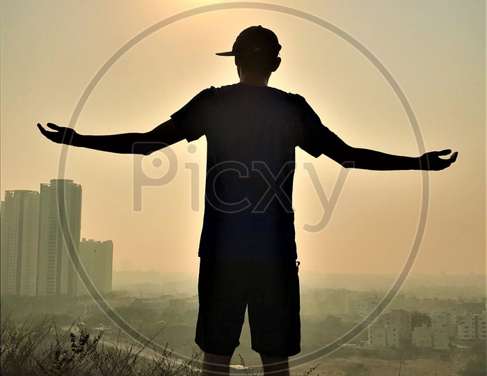 Silhouette of a Man Standing On a Rock Hill Over a Sun in Background